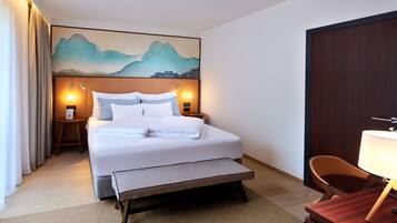 Ein ordentlich eingerichtetes Hotelzimmer mit einem großen Bett, Nachttischen mit Lampen, einem Schreibtisch mit Stuhl und einem Bild an der Wand.