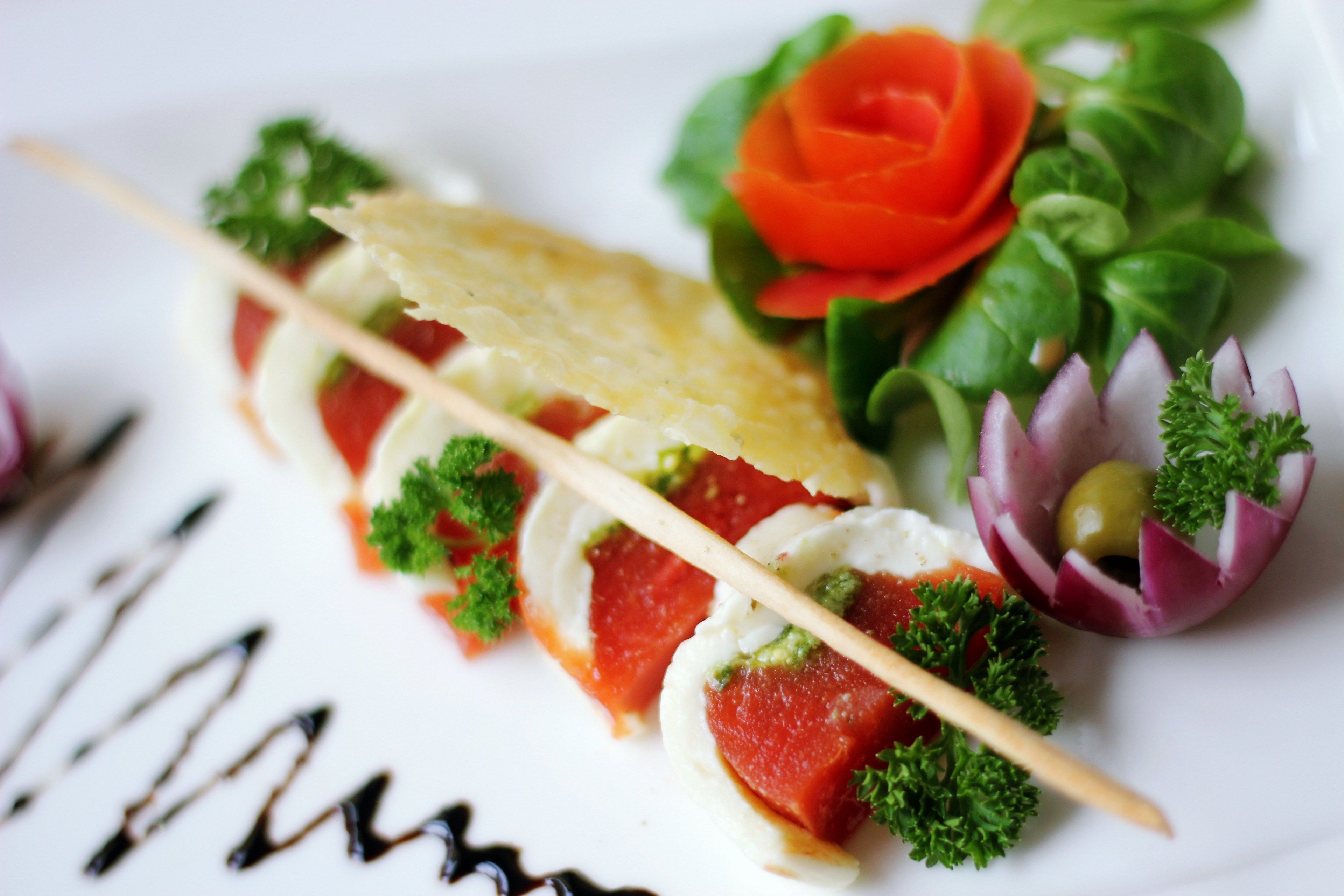 A plate with a food arrangement including a toothpick, a red tomato slice, a green leaf, and a small red onion piece.