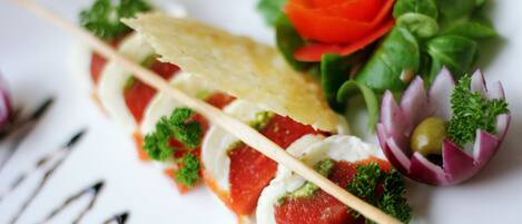 A plate with a food arrangement including a toothpick, a red tomato slice, a green leaf, and a small red onion piece.