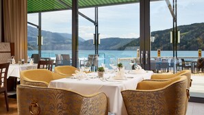 A restaurant with tables set for dining, large windows offering a view of the sea and mountains. - Seeglück Hotel Forelle Superior (Millstatt)