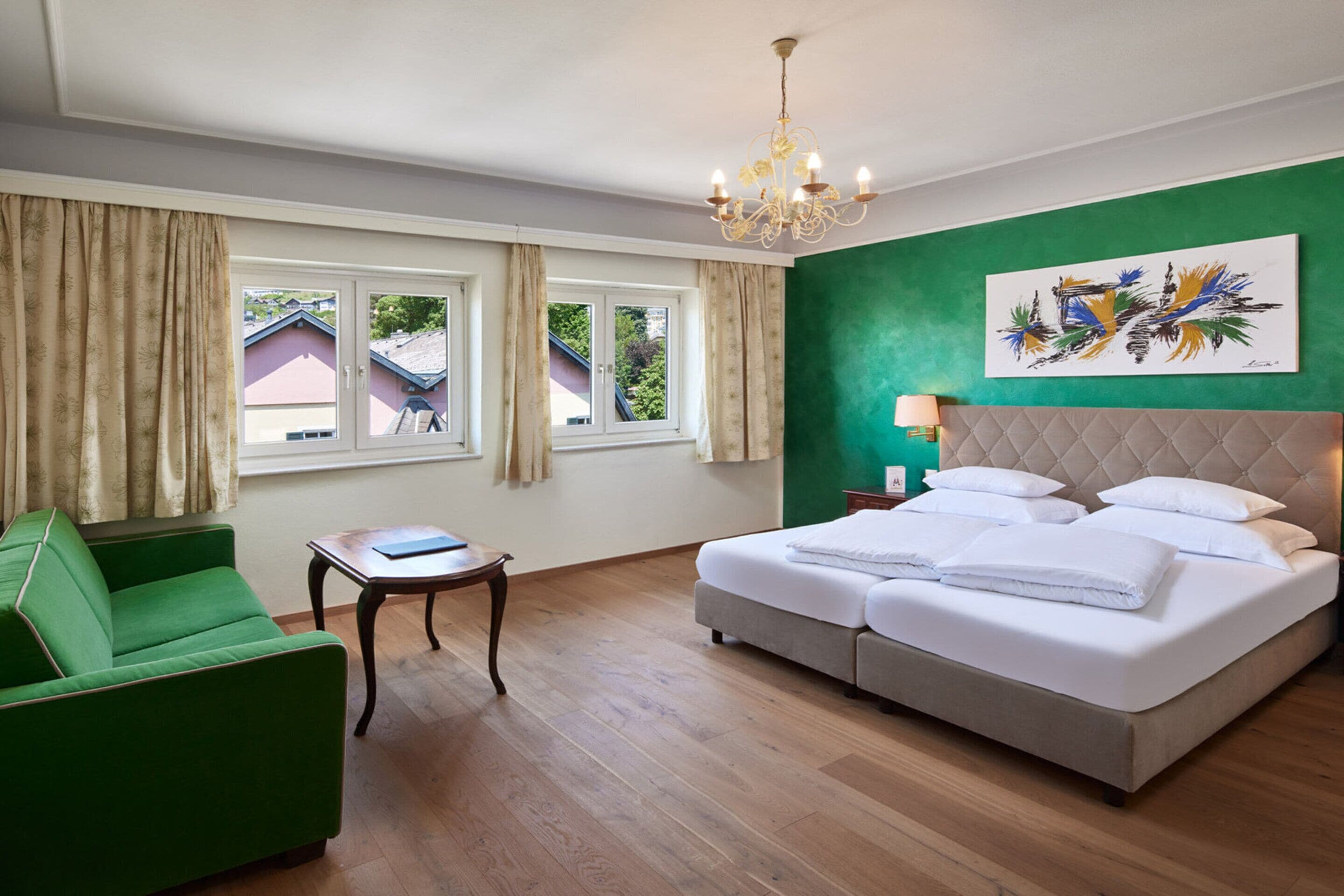 Una habitación de hotel con una cama, un sillón verde, una mesita y una ventana con cortinas.