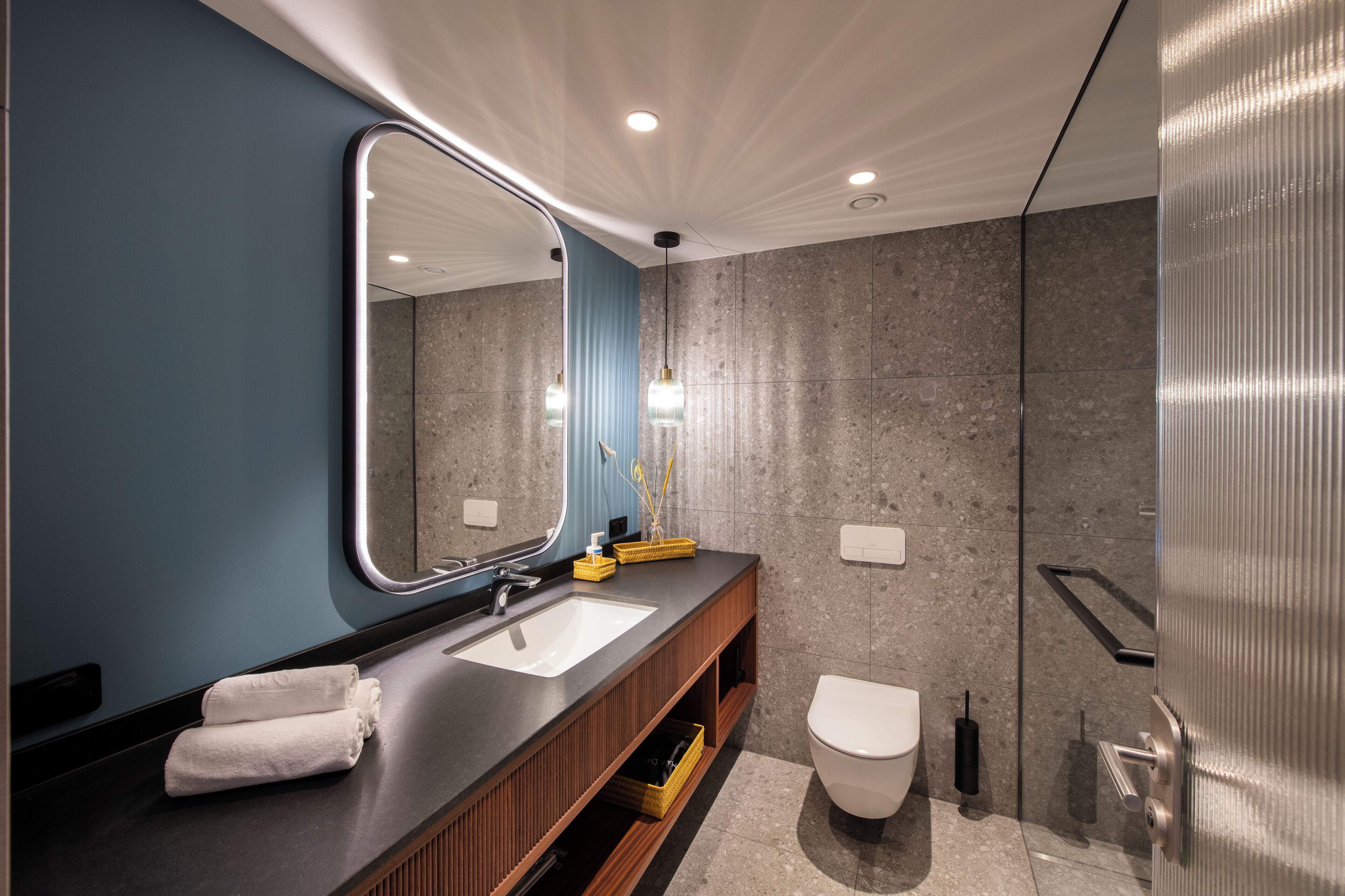A modern bathroom with a large mirror, a sink, a toilet, and a shower area.