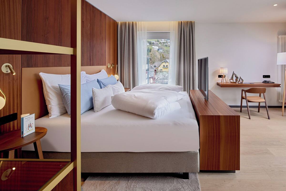 A modern hotel room with a large bed, a desk, and a view of the outside.