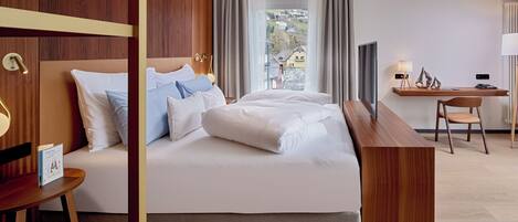 A modern hotel room with a large bed, a desk, and a view of the outside.