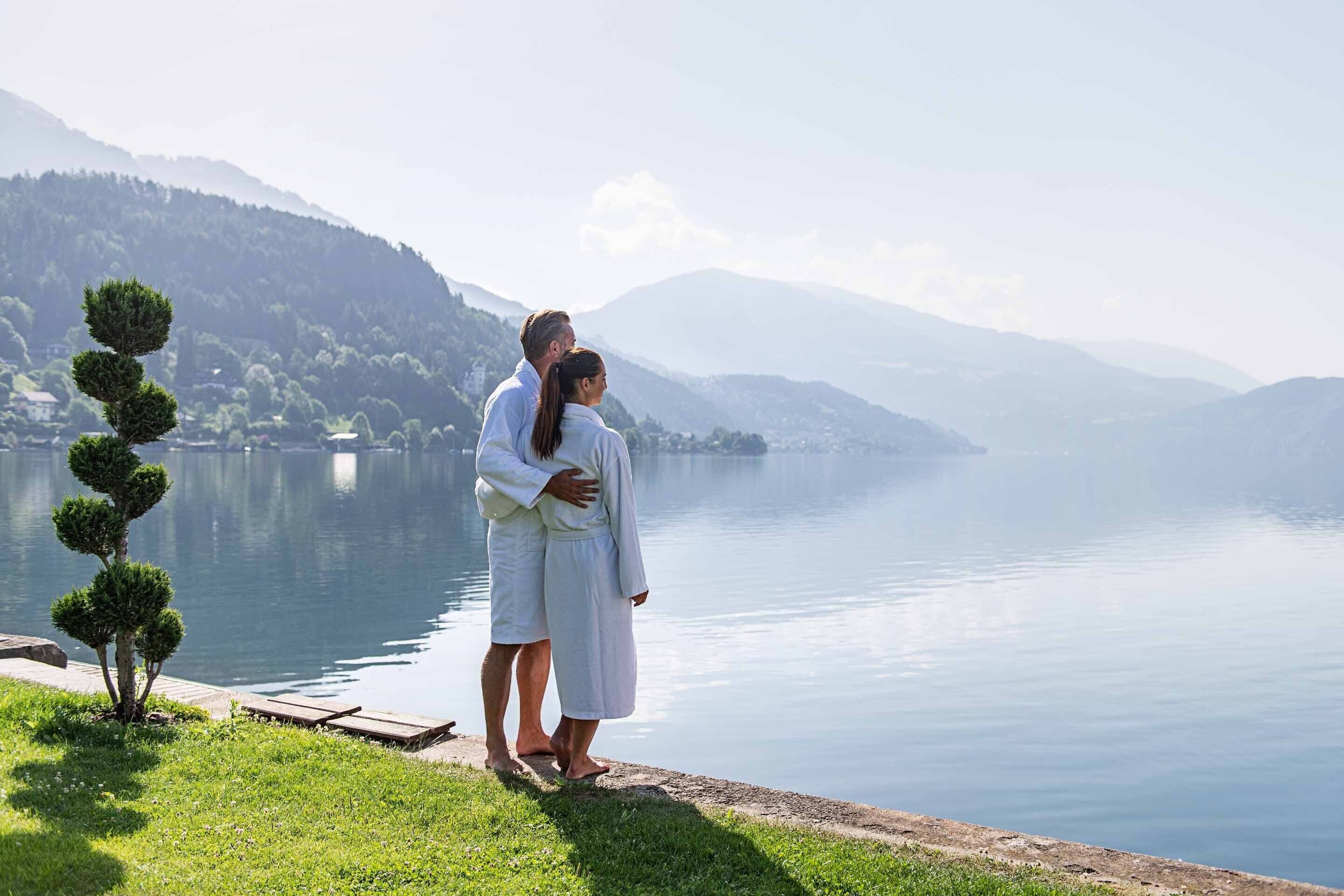 A couple embracing by a lakeside with a mountain backdrop.