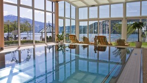 A large indoor swimming pool with clear views of a lake and mountains through large windows. - Seeglück Hotel Forelle Superior (Millstatt)