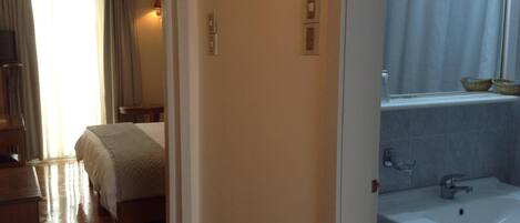 Quarto de hotel com cama, mesa de cabeceira, espelho, pia e janela com cortinas.
