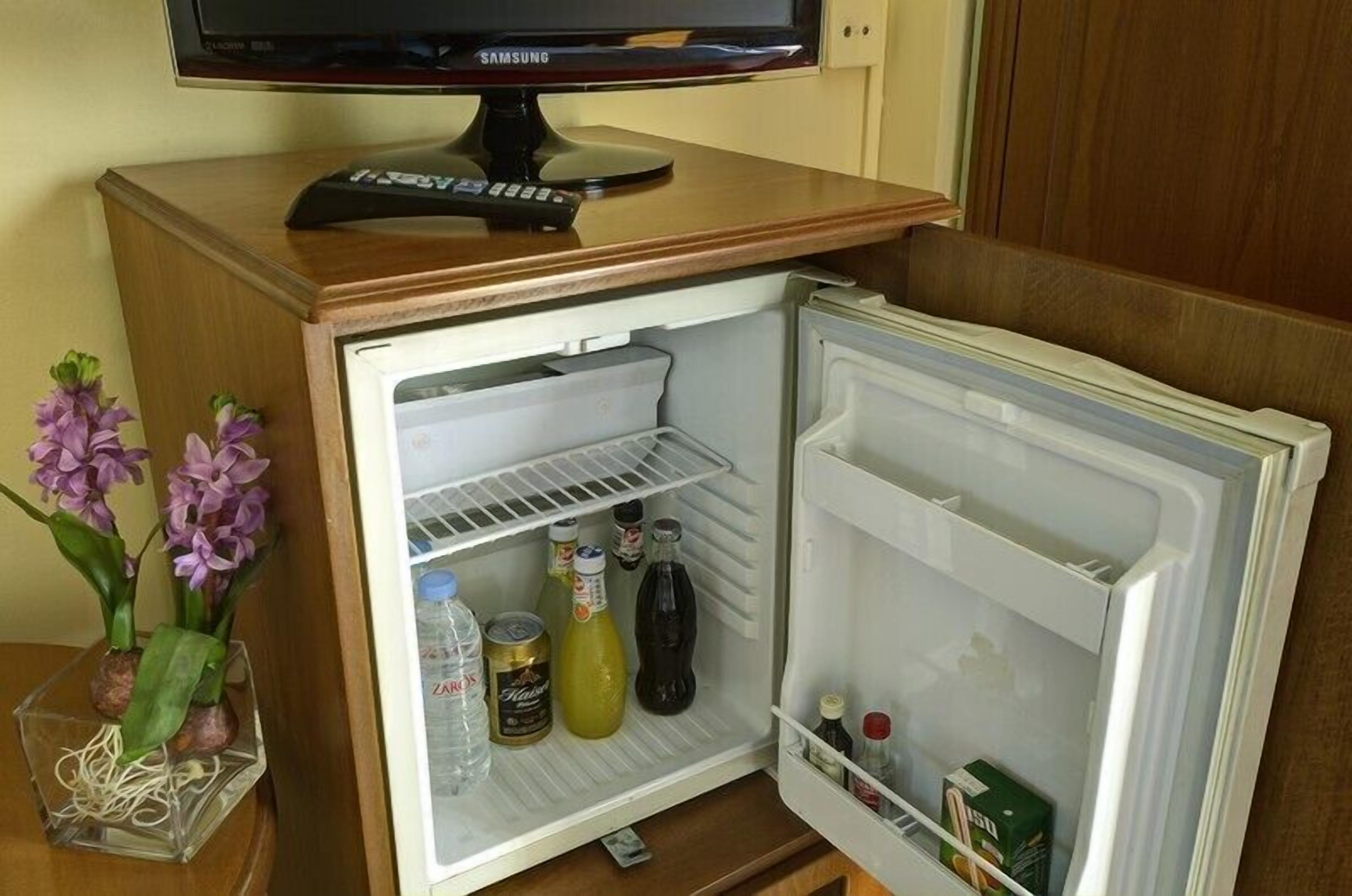 Un refrigerador compacto con un televisor Samsung encima, que contiene bebidas y condimentos.