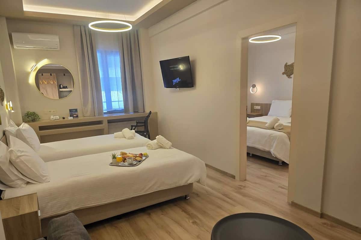 Una habitación de hotel moderna con dos camas, un televisor, un espejo, una mesita con desayuno y vistas a la ciudad.