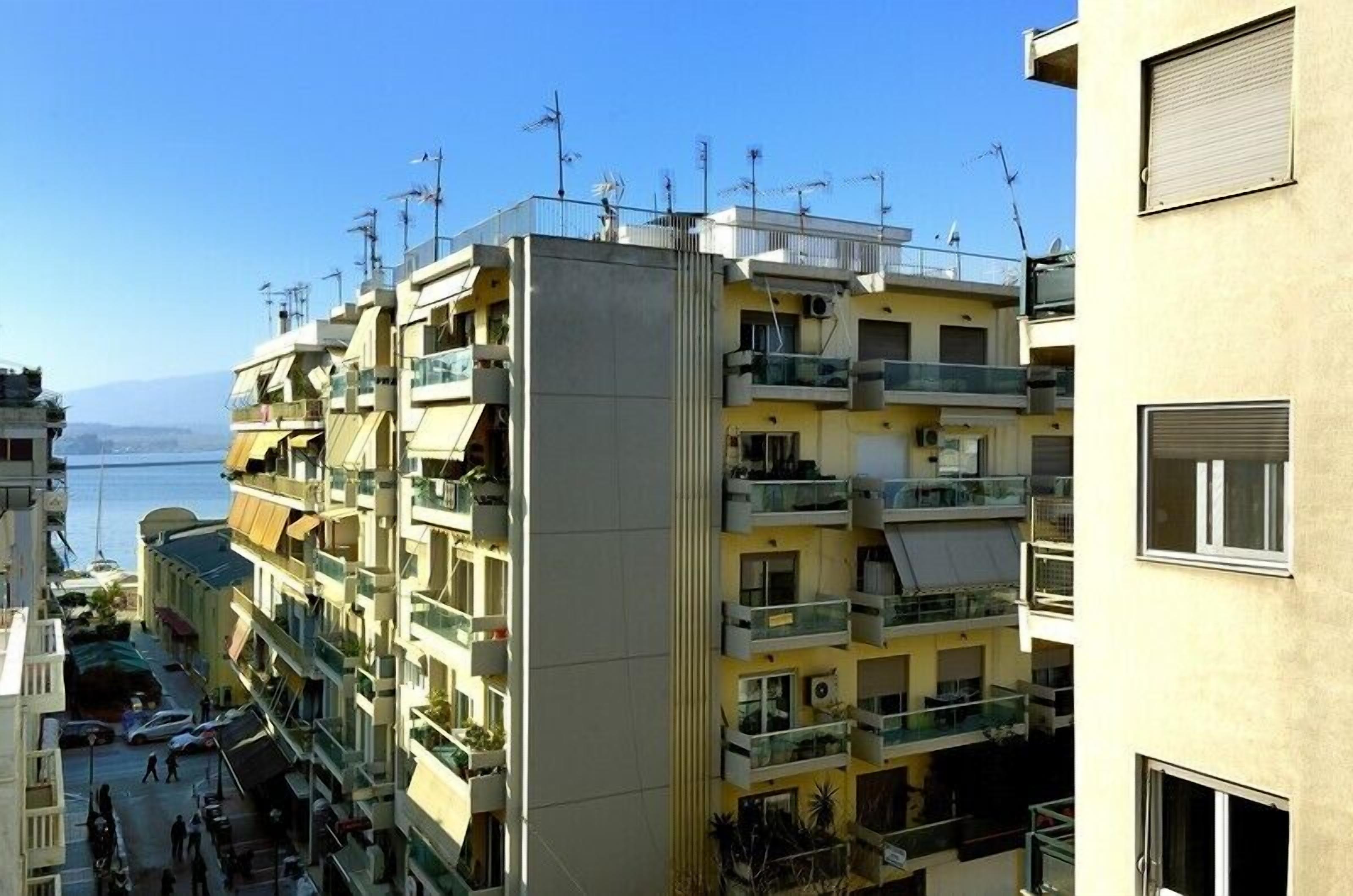 A multi-story residential building with balconies, a clear view of the sea, and a pedestrian street below.