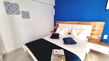 Quarto moderno com uma cama grande, cabeceira branca e paredes azuis.