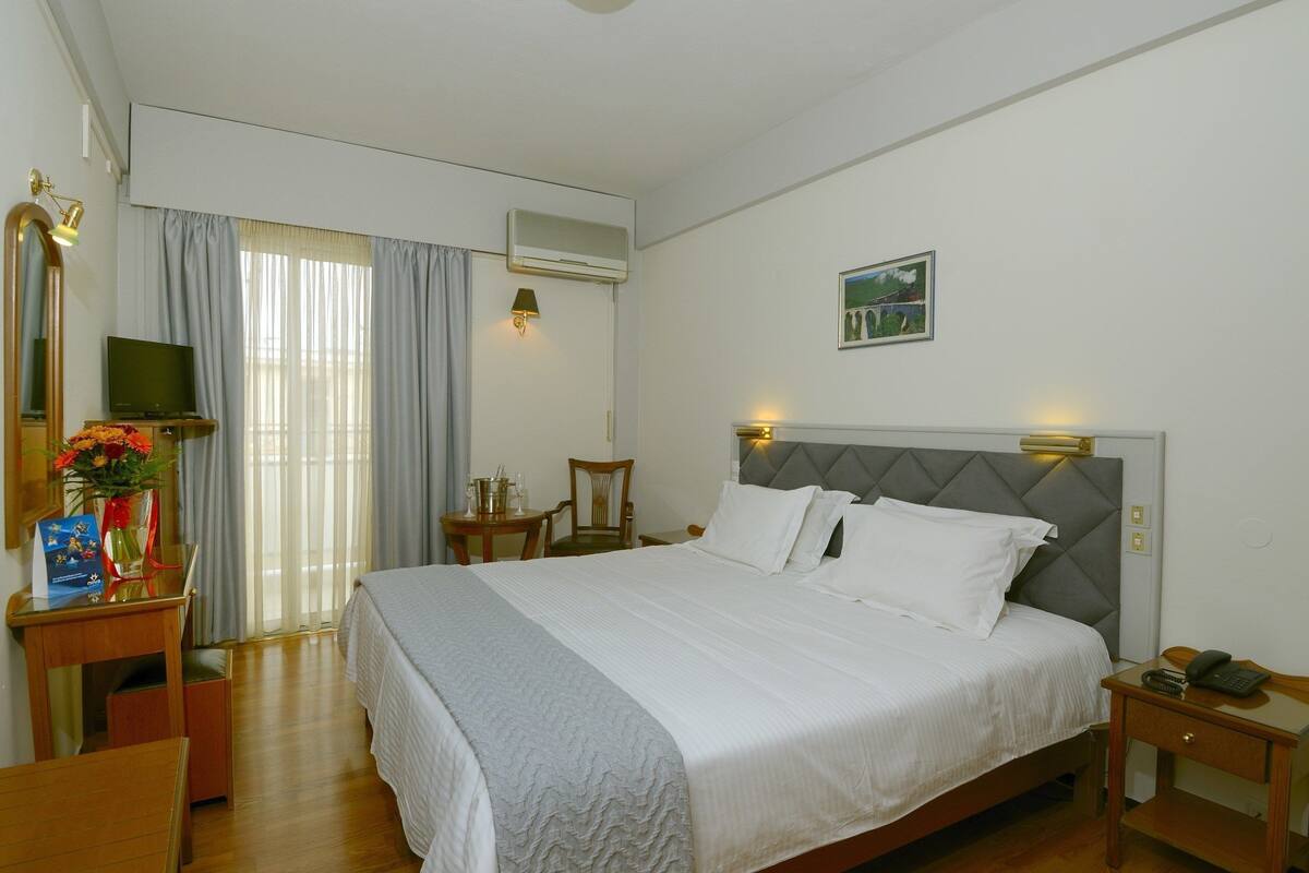 Habitación de hotel con cama, escritorio, silla, televisor, aire acondicionado y un cuadro en la pared.