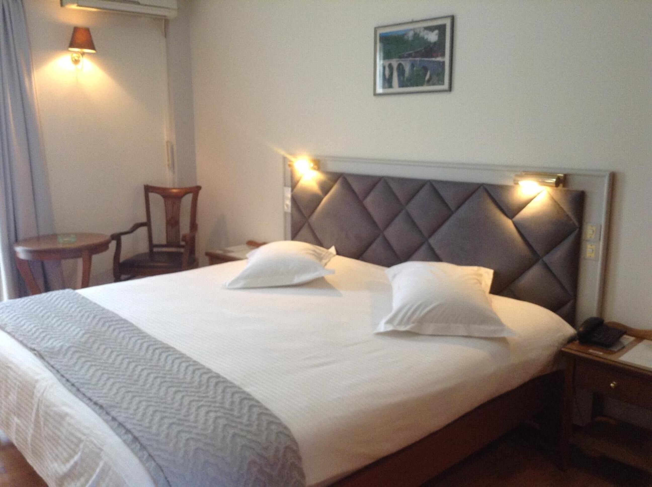 Een hotelkamer met een groot bed, twee nachtkastjes, een stoel en een aan de muur hangend schilderij.