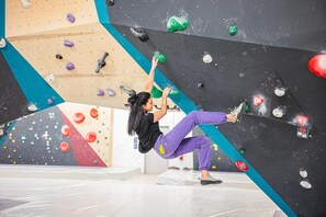 Une personne escalade un mur d’escalade intérieur multicolore, doté de différentes prises.