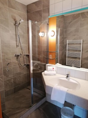 Un bagno moderno con cabina doccia in vetro, un lavandino bianco e un porta asciugamani.