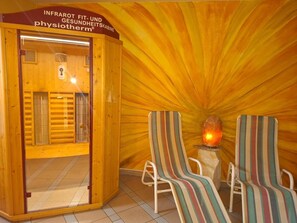 Un sauna avec des murs en bois, une porte en verre, deux chaises à rayures et un poêle en pierre.