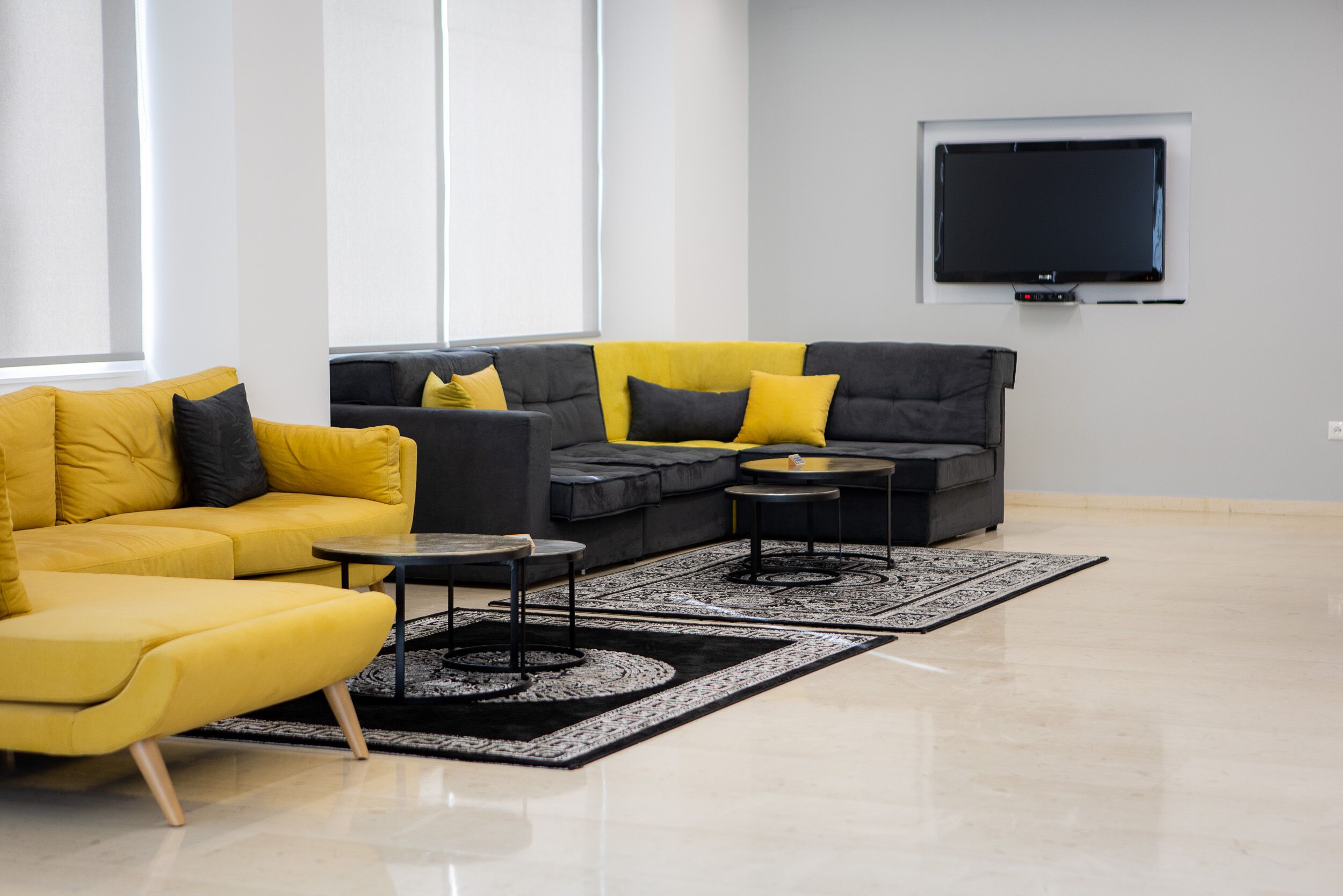Una sala de estar moderna con un sofá amarillo, un sofá modular gris y un televisor negro en la pared.