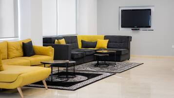 Una sala de estar moderna con un sofá amarillo, un sofá modular gris y un televisor negro en la pared.