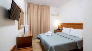 Una habitación de hotel con una cama, televisión montada en la pared, una mesita de noche y una ventana con cortinas.
