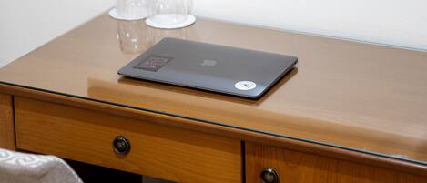 A wooden desk with a laptop, two clear glasses, and a mirror reflecting a chair and curtains.