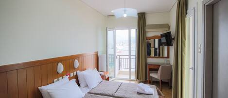 A hotel room with two beds, a desk, a chair, and a view of the city through the balcony doors.