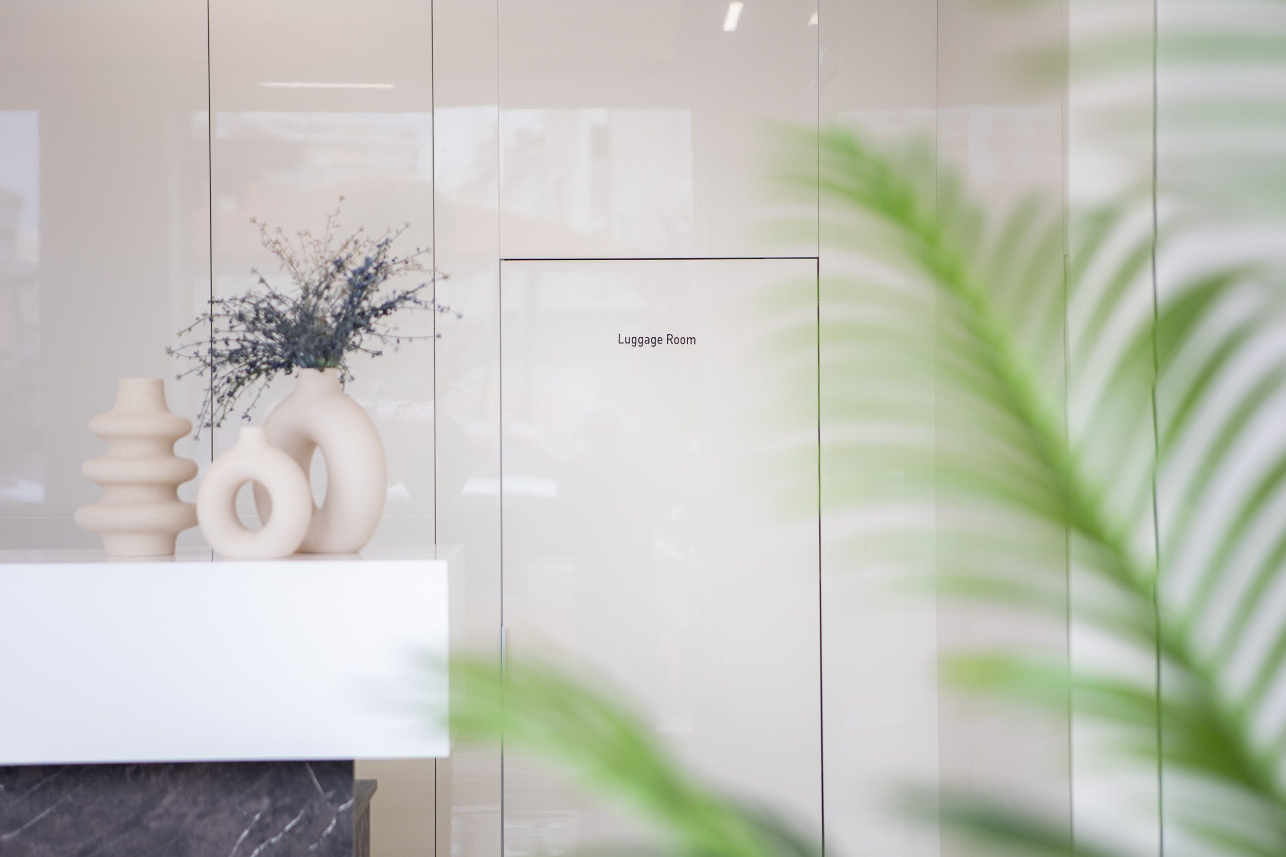 A modern room with a marble countertop, a vase with dried flowers, and a sign indicating the luggage room.