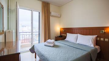 A hotel room with a bed, a desk, a window with curtains, and an air conditioning unit.
