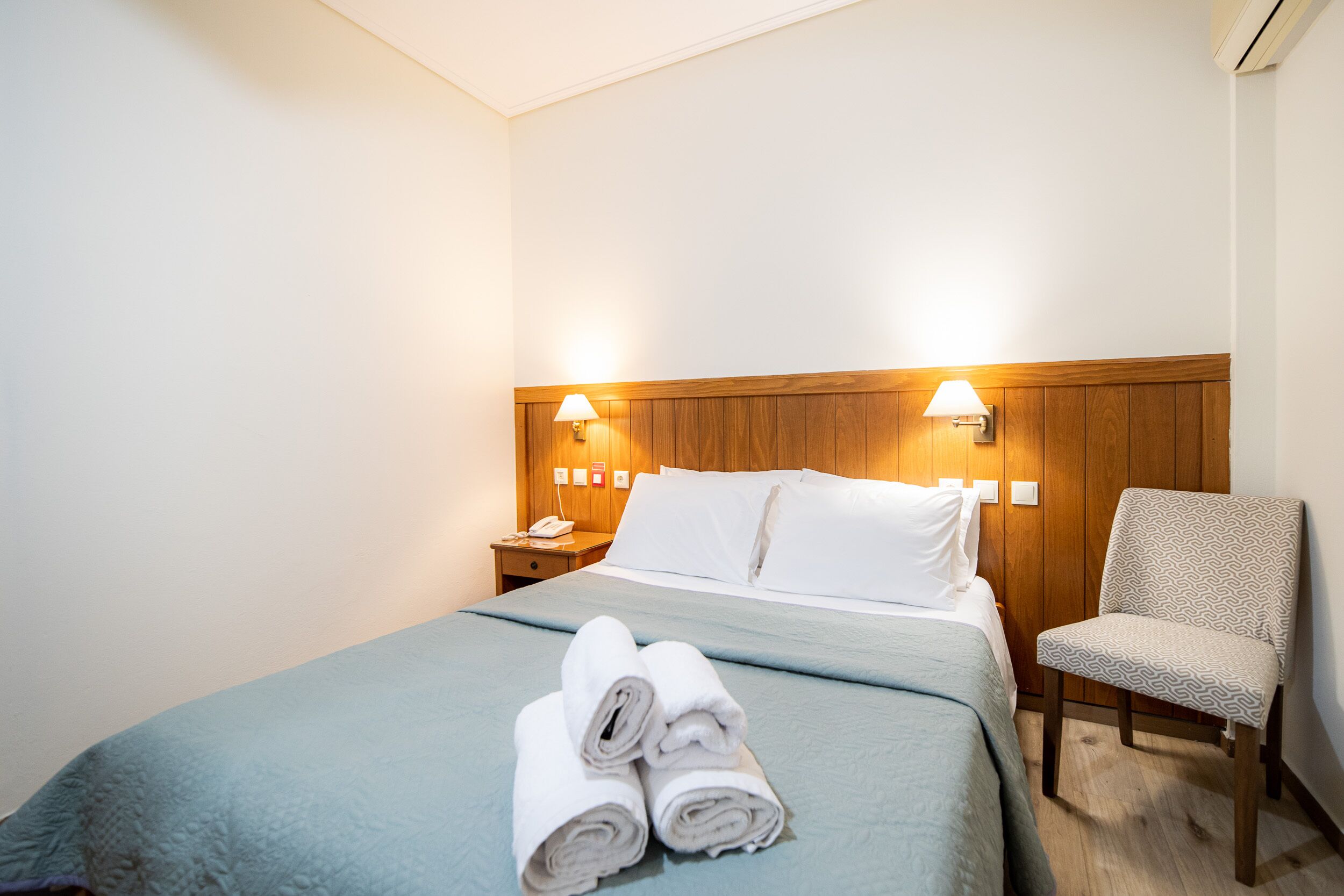 Ein Hotelzimmer mit einem Bett, einem Sessel, einem Nachttisch und einer Lampe.