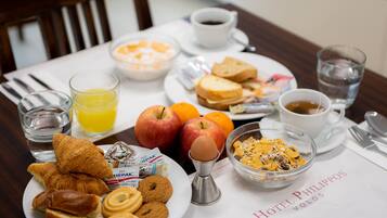 Una mesa de desayuno con cruasanes, manzanas, zumo de naranja y cereales.