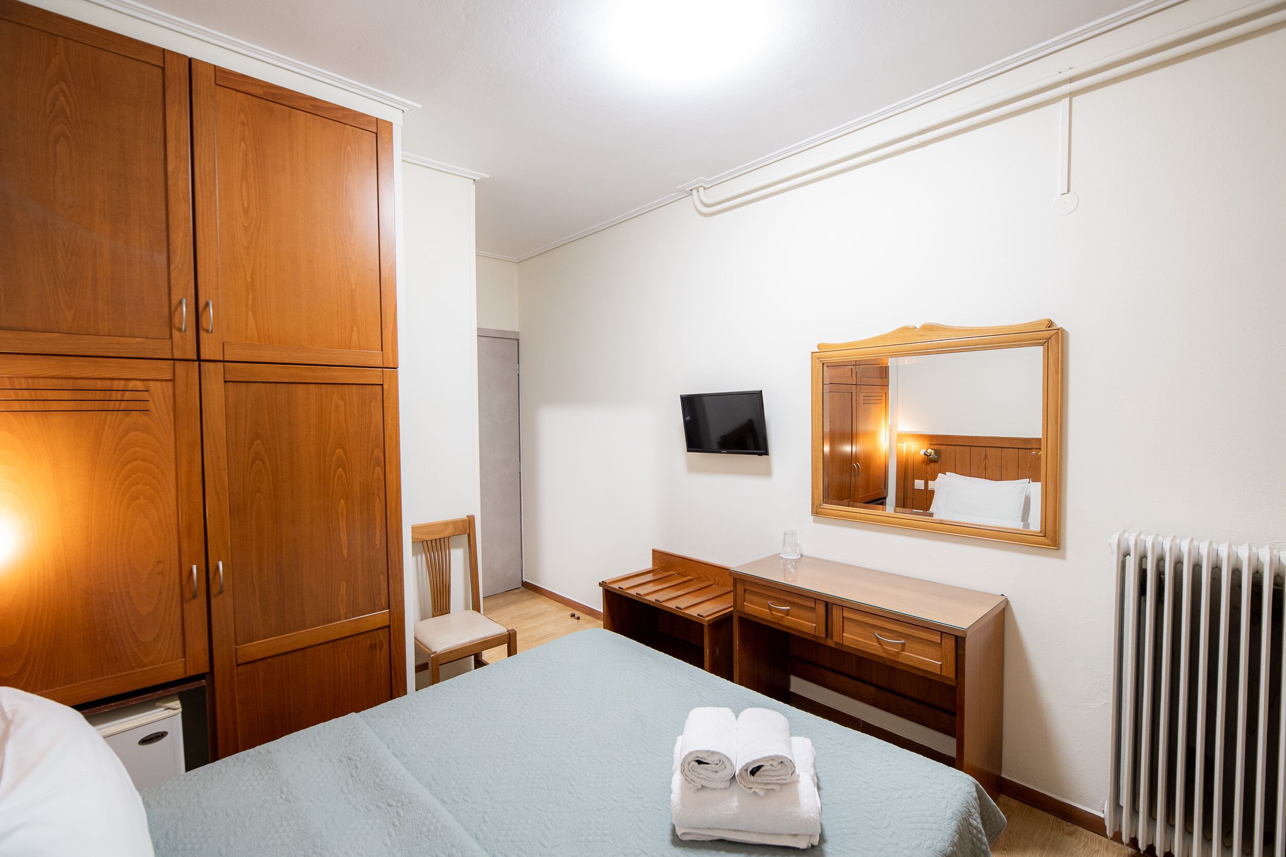 Habitación de hotel con cama, armario de madera, escritorio, silla y televisor.