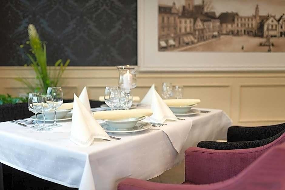 A dining table set with white tablecloths, glassware, and napkins, with a framed picture on the wall behind.