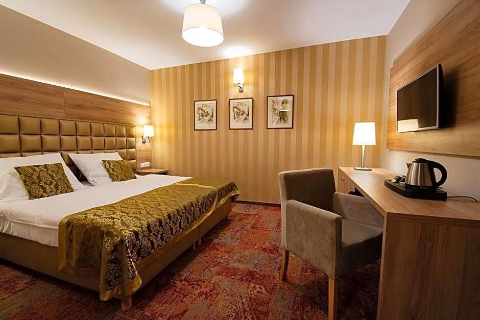 Ein Hotelzimmer mit einem großen Bett, einem Schreibtisch mit Stuhl, einem Fernseher und gerahmten Bildern an der Wand.