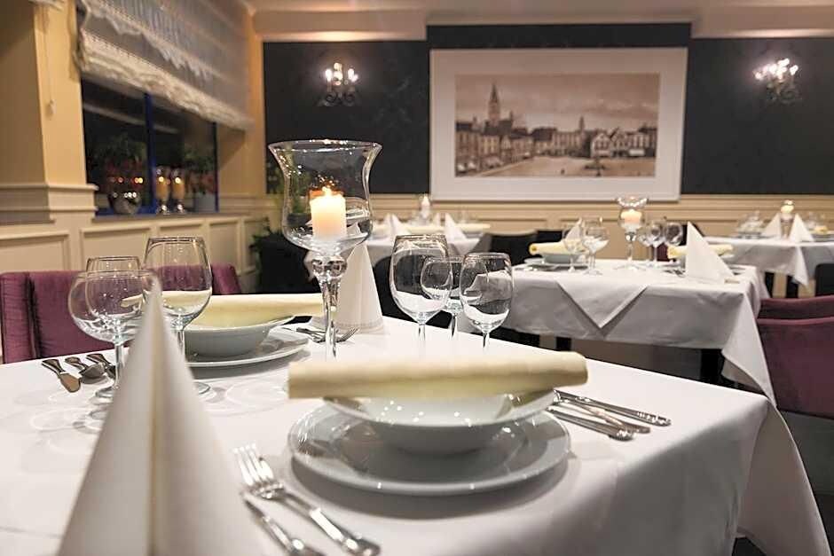 Ein Restaurantambiente mit gedeckten Tischen, weißen Tischdecken, Tellern, Besteck und Gläsern.