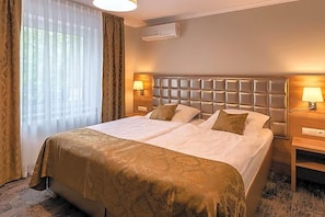 A hotel room with a large bed, two bedside tables, a headboard, and a window with curtains.