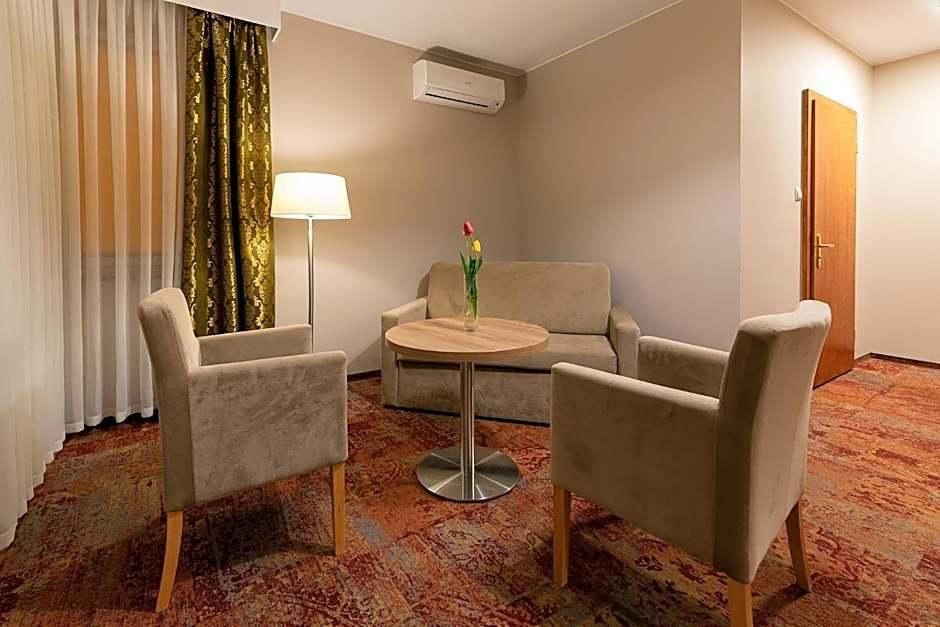 Ein Hotelzimmer mit einer Couch, zwei Sesseln, einem kleinen runden Tisch, einer Lampe und einer Tür.