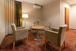 A hotel room with a sofa, two armchairs, a small round table, a lamp, and a door.