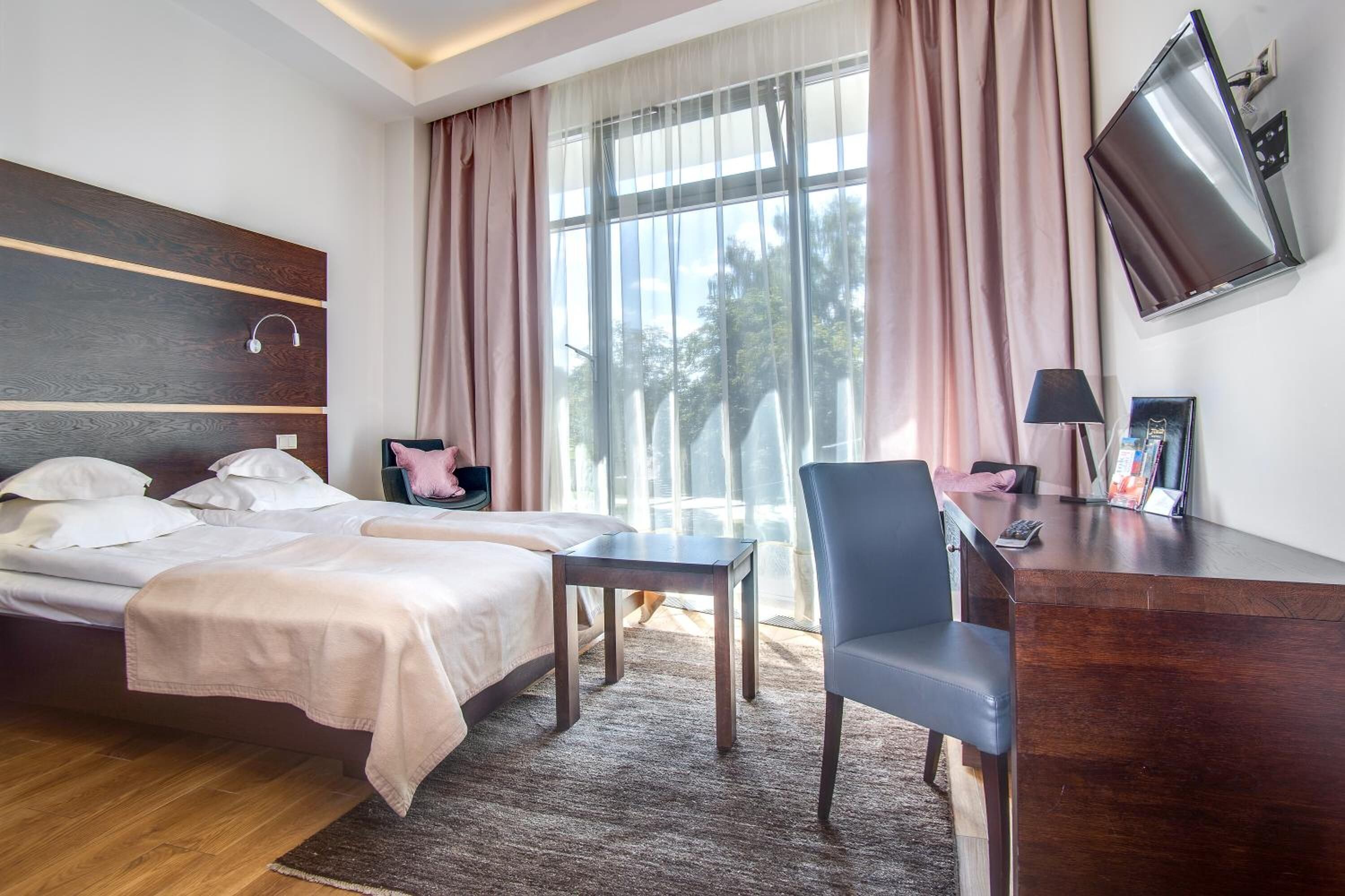 A hotel room with a bed, a desk, a chair, a TV, and a window with curtains.
