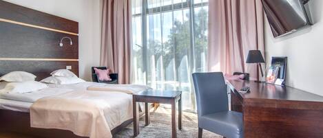Habitación de hotel con cama, escritorio, silla, televisión y ventana con cortinas.