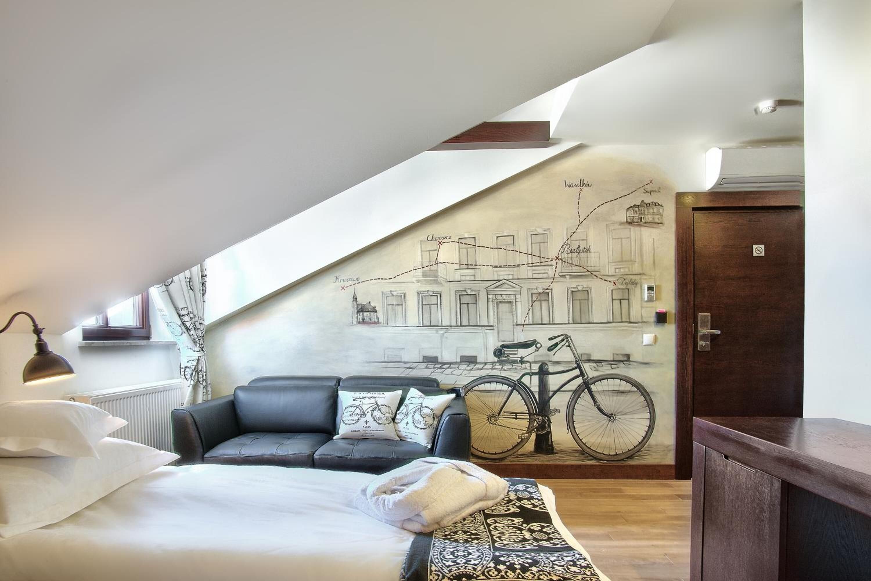 A bedroom with a bed, a sofa, a bicycle mural, and a wooden cabinet.