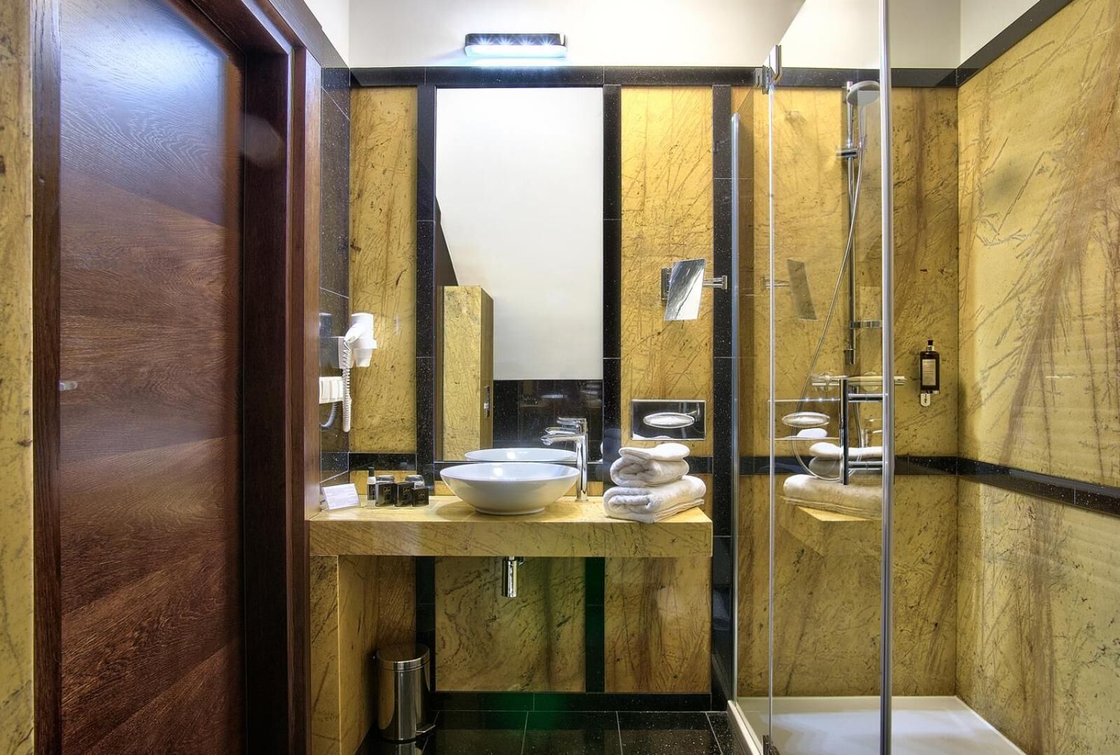 A bathroom with a marble vanity, a sink, a mirror, a towel rack, and a glass shower enclosure.