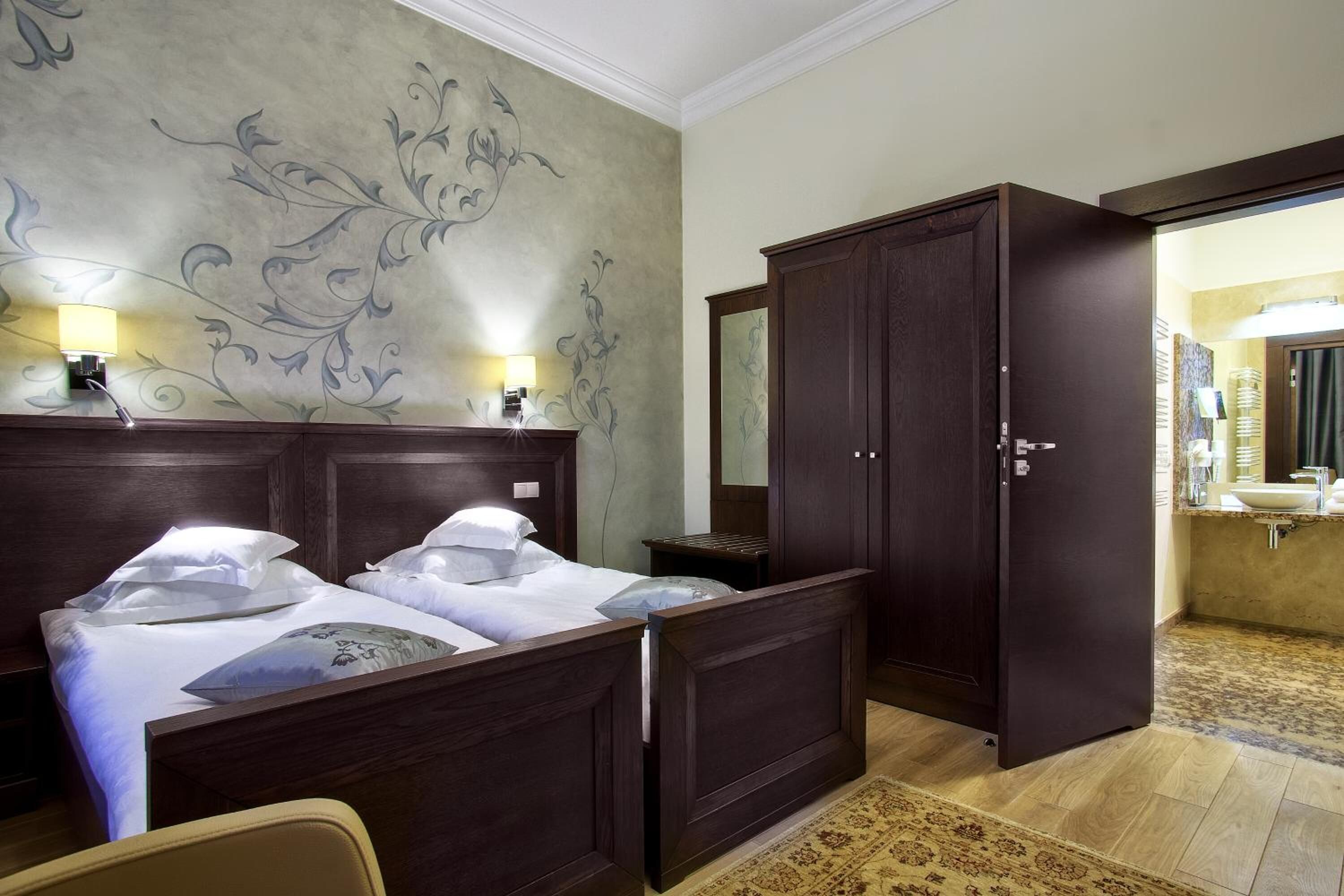 Camera d'albergo con due letti, un ampio guardaroba, uno specchio e bagno visibile attraverso una porta aperta.