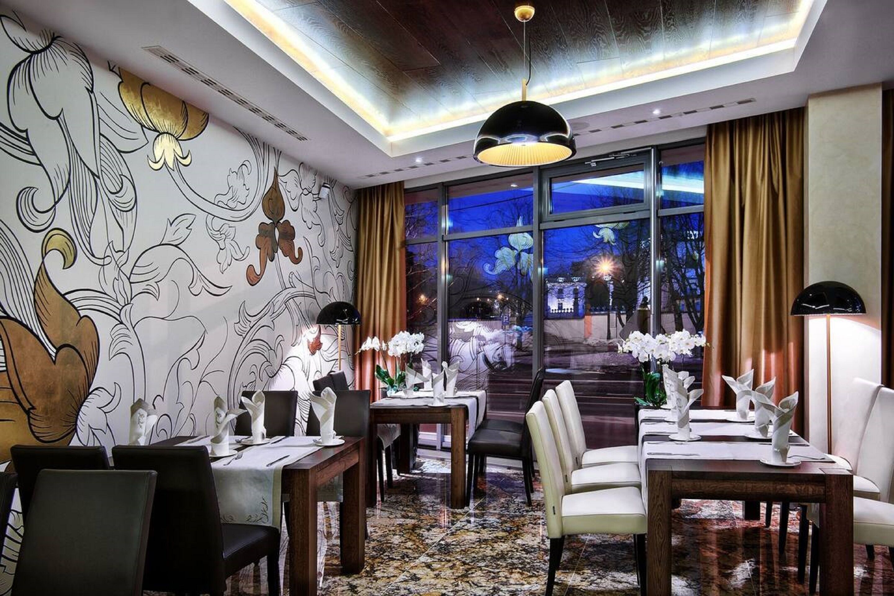 Un comedor con mesas dispuestas para el servicio, una araña y vistas de la ciudad de noche.