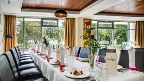 A restaurant with a long table set for a meal, large windows, and a view of trees. - Hotel Aristo (Bialystok)