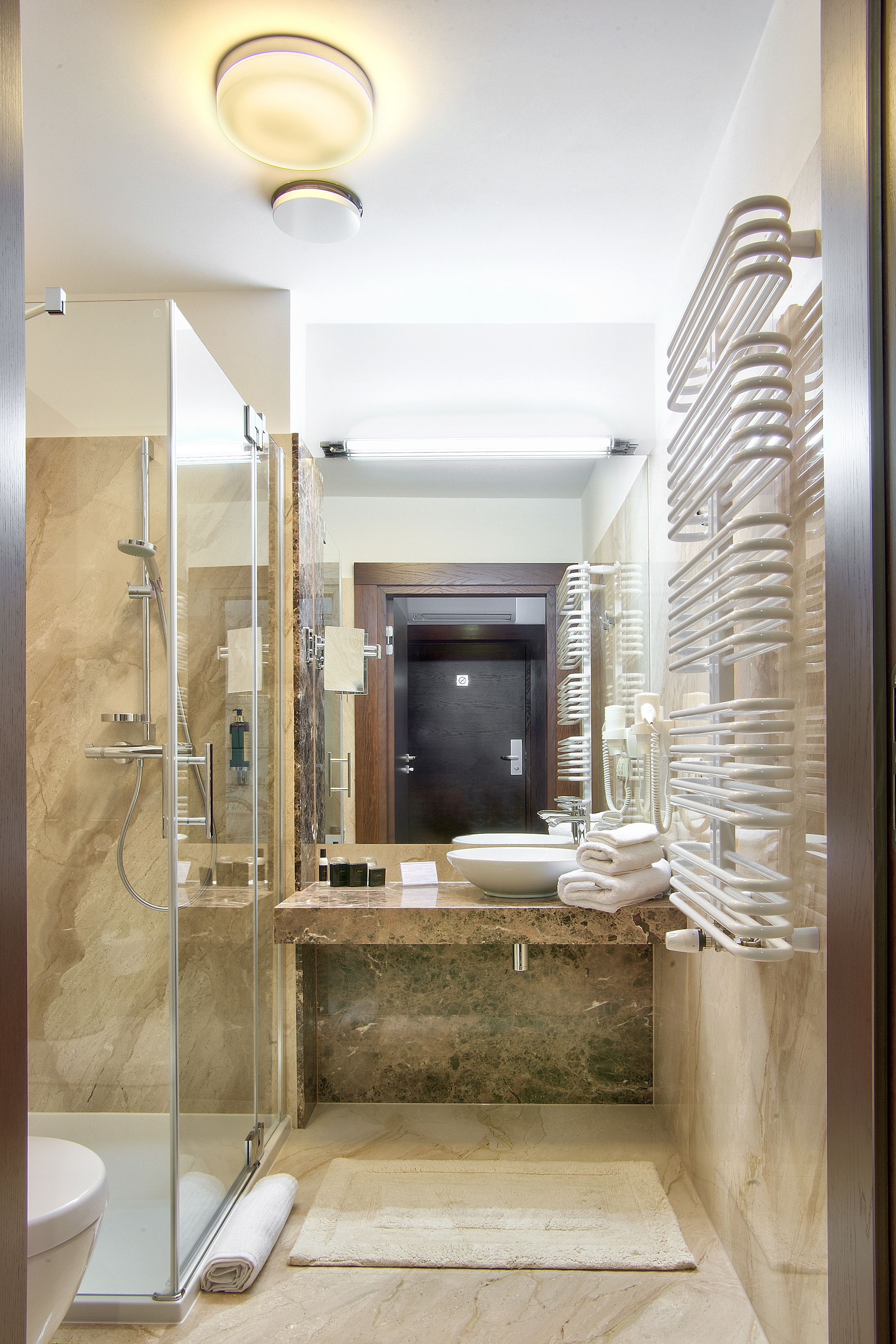 Un baño moderno con ducha envuelta en vidrio, un lavamanos con encimera de mármol y un perchero con varias toallas.