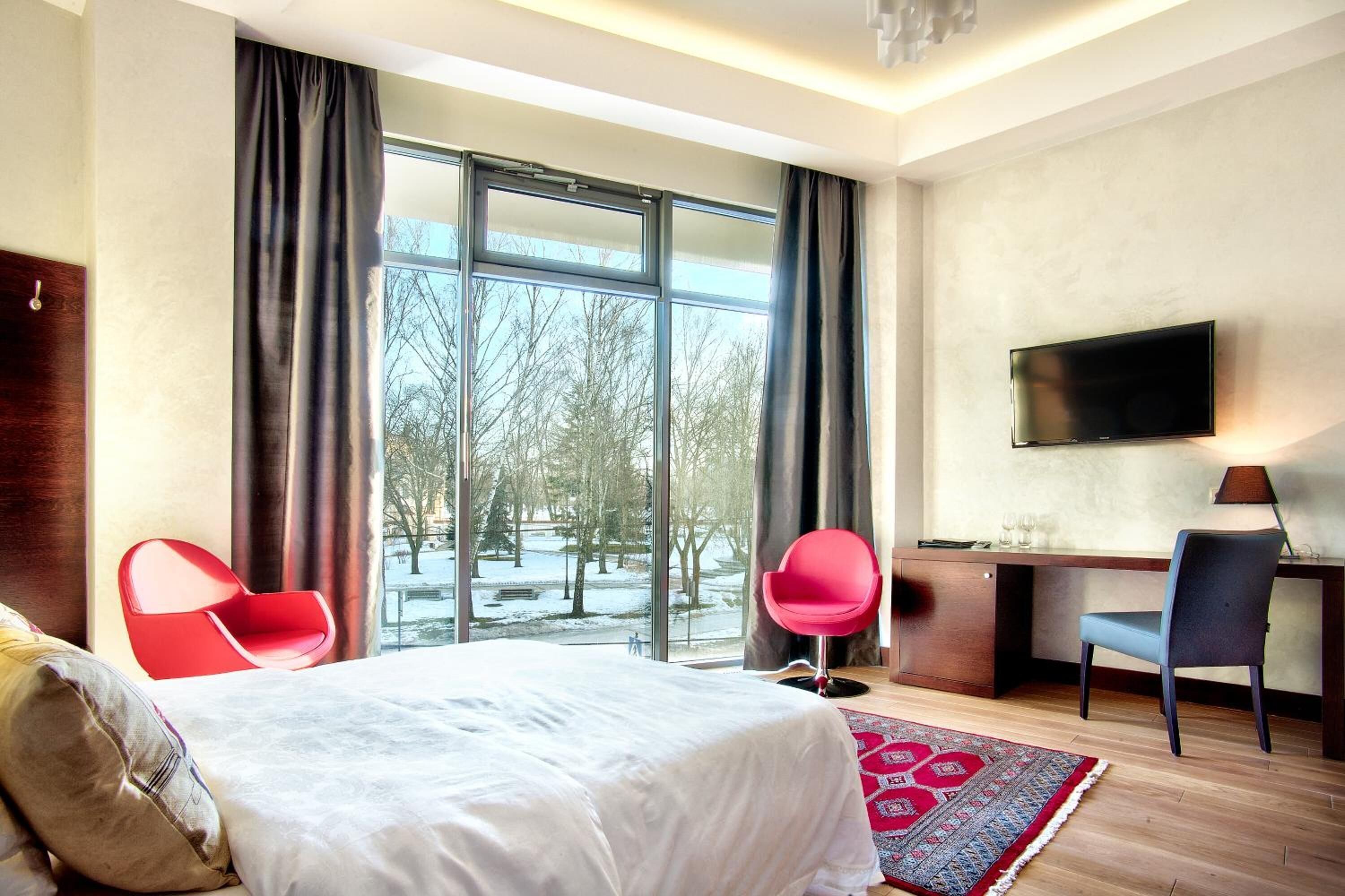 Quarto de hotel com uma cama grande, uma escrivaninha, duas cadeiras, uma televisão e vista para um parque nevado.