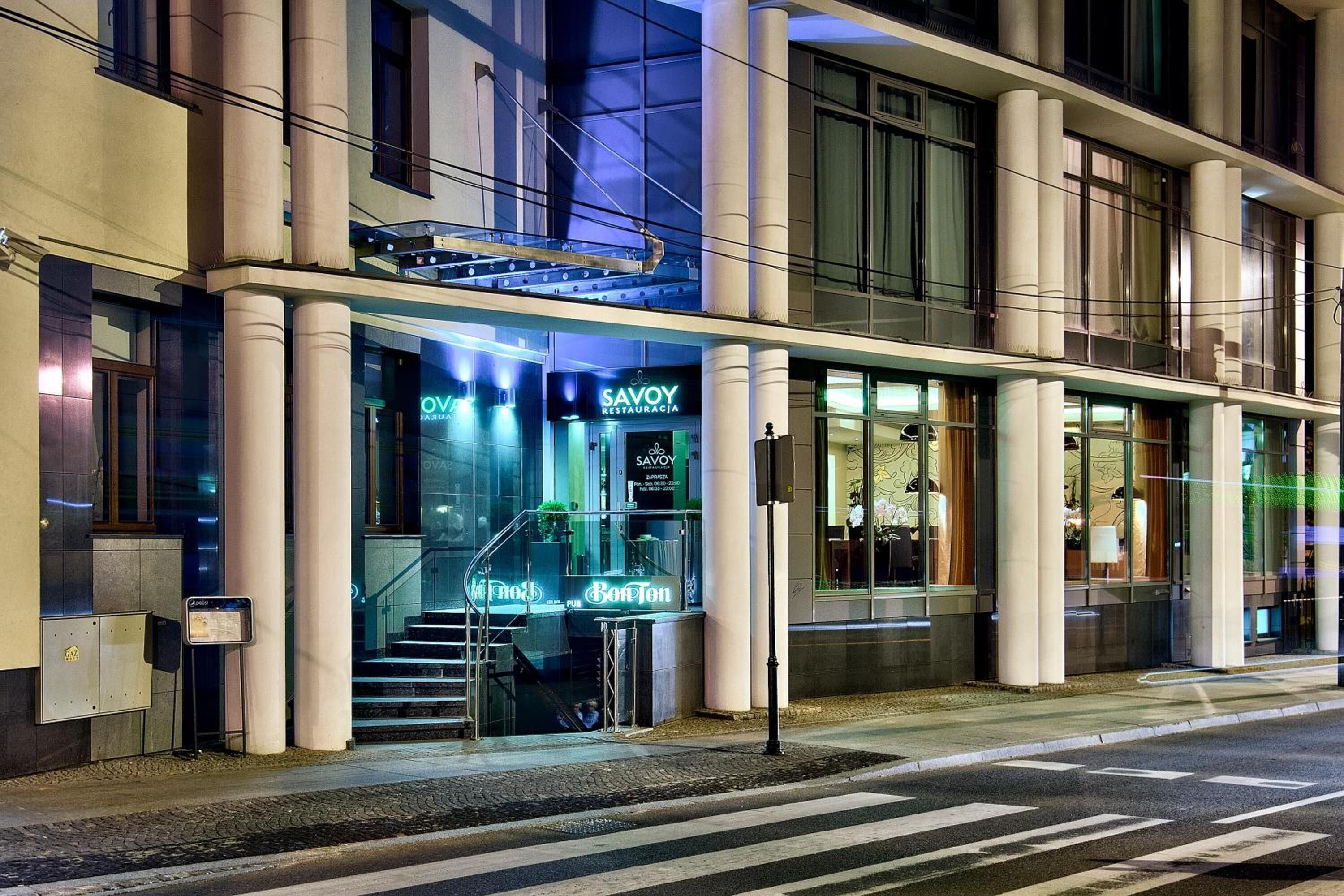 A modern building with a glass facade, a visible entrance with steps, and signage for 'Savoy Restaurante'.