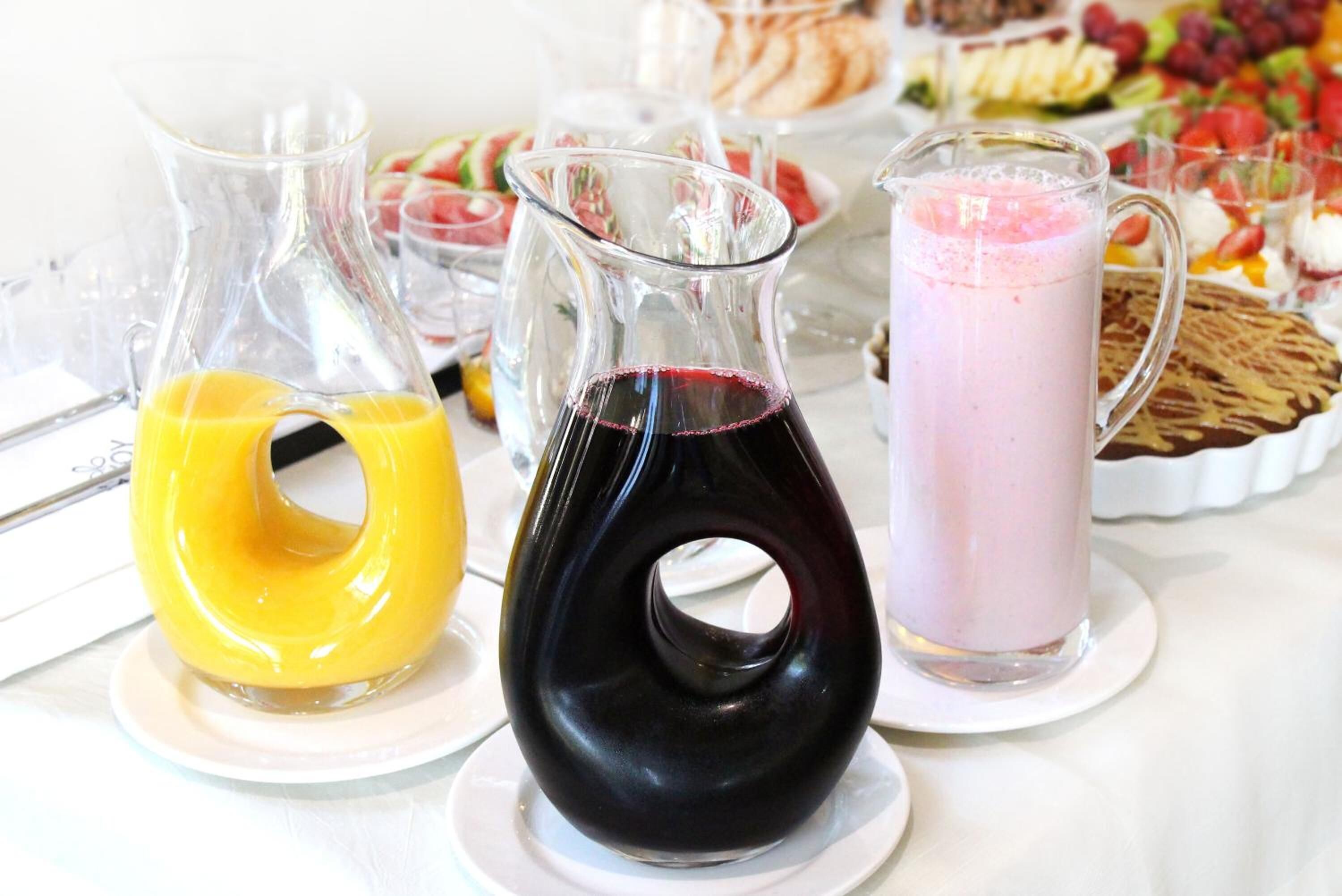 Tres jarras de bebidas sobre una mesa, con varios alimentos al fondo.