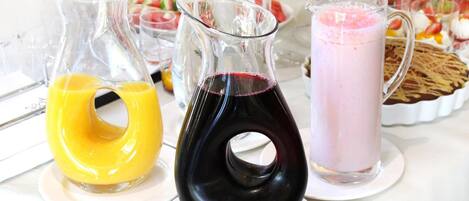 Tres jarras de bebidas sobre una mesa, con varios alimentos al fondo.