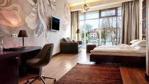 A modern hotel room with a large bed, a desk with a chair, a sofa, and a TV mounted on the wall. - Hotel Aristo (Bialystok)