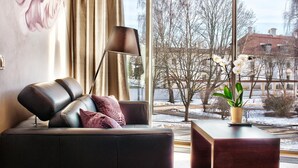 A modern living room with a leather sofa, a floor lamp, and a view of a snowy landscape through large windows. - Hotel Aristo (Bialystok)